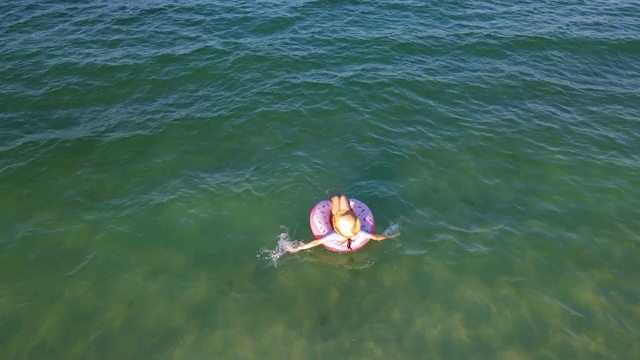 女人游泳和漂浮在海边的水与甜甜圈浮动鸟瞰图视频素材