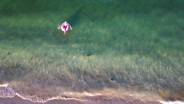 女人游泳和漂浮在海边的水与甜甜圈浮动鸟瞰图视频素材