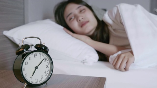 一名亚洲妇女因闹钟的敲响而醒来的场景。然后她把闹钟关掉，继续睡觉视频素材