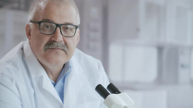 一个男医生在实验室里用显微镜看着照相机的肖像视频下载