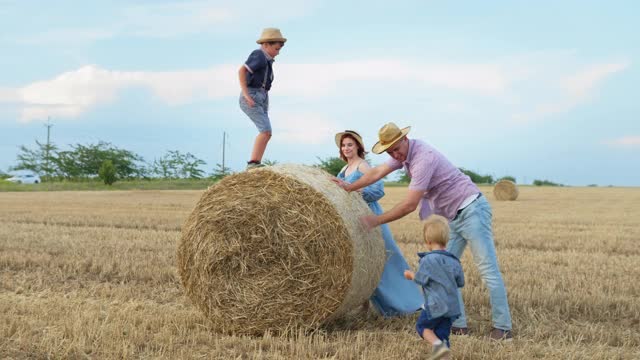 家庭乐趣，快乐的父母有乐趣与他们的男性孩子玩捆干草在麦田在农村周末视频下载