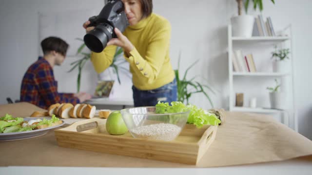 近距离跟踪拍摄的女性摄影师拍摄的食物放在桌子上，并被男制片人建议查看笔记本电脑上的照片视频下载