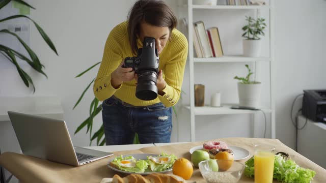 职业女性摄影师在办公室桌子上拍摄食物背景照片，并在笔记本电脑上查看图片视频下载