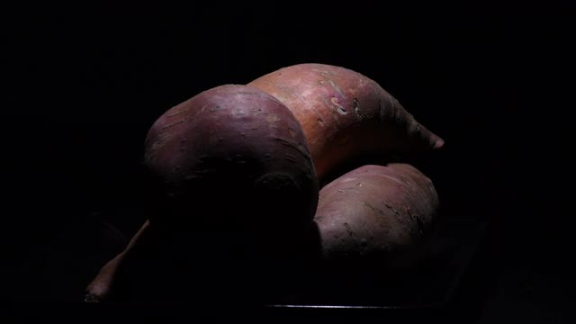 在黑色背景上旋转的生红薯。番薯甘薯视频素材