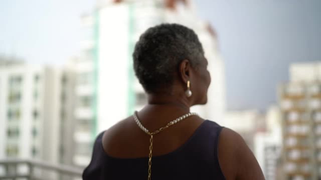 一个年长的女人在公寓的门廊看风景的后视图视频素材