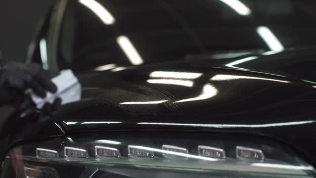 汽车装饰-曼在黑色汽车上应用纳米保护涂层或蜡。用液体玻璃上光剂覆盖汽车引擎盖视频素材