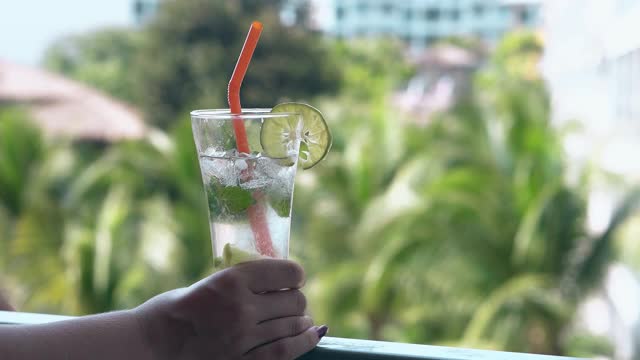 在酒店的阳台上，女孩拿着装有冰冻饮料的杯子视频素材