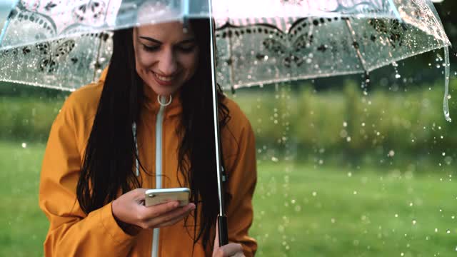 一名年轻女子在雨中使用智能手机时微笑视频素材
