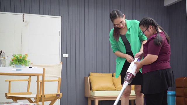 一位亚洲老师教患有唐氏综合症的女学生如何用手持式吸尘器打扫教室。儿童教育理念要可持续，女童权力要社会责任。视频下载