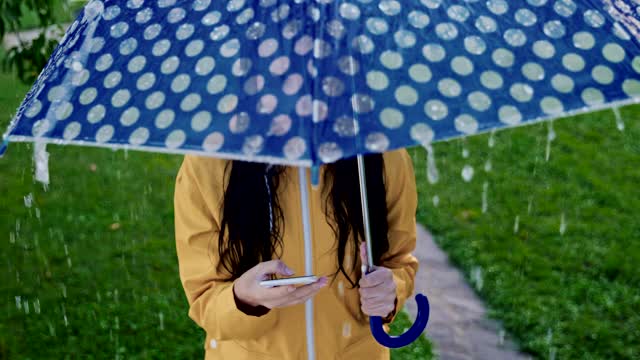 一个穿着雨衣在雨中使用智能手机的女人视频素材