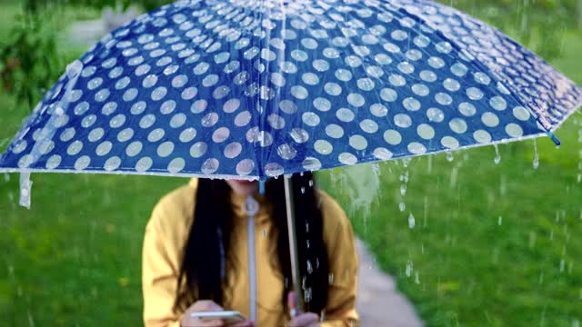 一名年轻女子在雨中玩智能手机视频素材