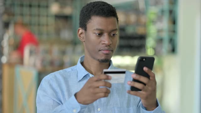 年轻的非洲男子用智能手机在线支付的肖像视频素材