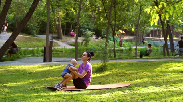 健身妇女在公园里锻炼，婴儿躺在她的小腿上视频下载