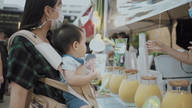 年轻的妈妈和她的儿子在泰国的街头小吃市场买甘蔗汁视频素材