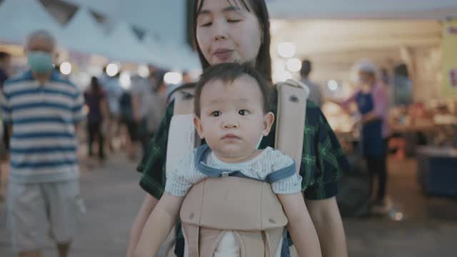 在泰国的街头小吃市场，一位年轻的母亲正在给她的儿子喂甘蔗汁视频素材