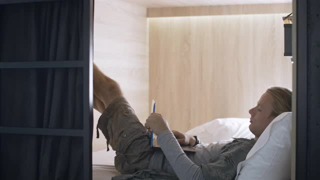 一个面目全非的男人的臭脚和另一个在低床上使用笔记本电脑的男人挂在一起。恼怒的白人男子在旅店或旅馆里上网并拉上窗帘的肖像。电影4k ProRes总部。视频素材