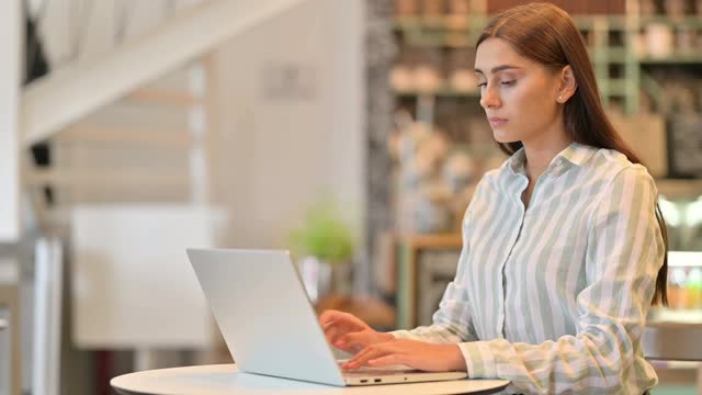 疲惫的年轻拉丁女人与笔记本电脑在咖啡馆背痛视频素材