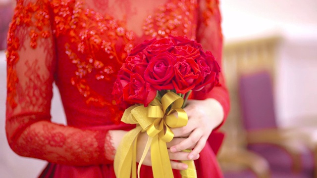 婚礼当天，新娘身着红色婚纱，手捧玫瑰花束视频下载