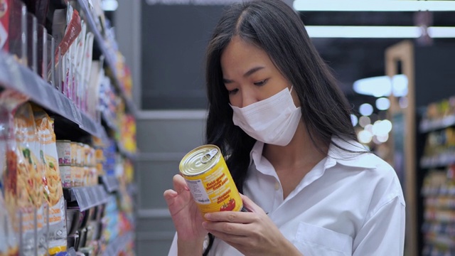新冠肺炎疫情期间，25岁的亚洲年轻女性戴着医用防护口罩在超市购买基本生活必需品。超市购物的概念。视频下载