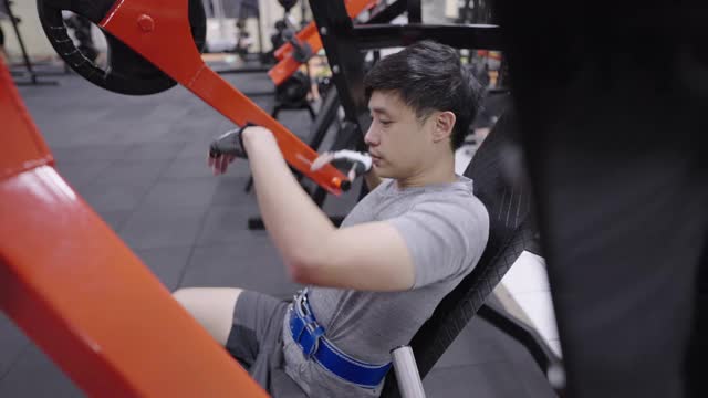 青年运动员在健身房里坐着的机器上做手臂和肩膀的锻炼。视频素材