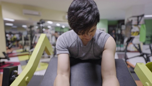 一个年轻人在健身俱乐部的健身器上锻炼时感到很累。视频素材