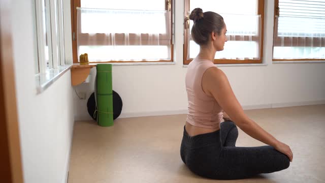 侧面的运动年轻女子在运动服练习瑜伽在地板上在家。高质量4k镜头视频素材