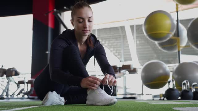 运动女性坐在地板上，穿着运动鞋系鞋带在健身馆视频素材