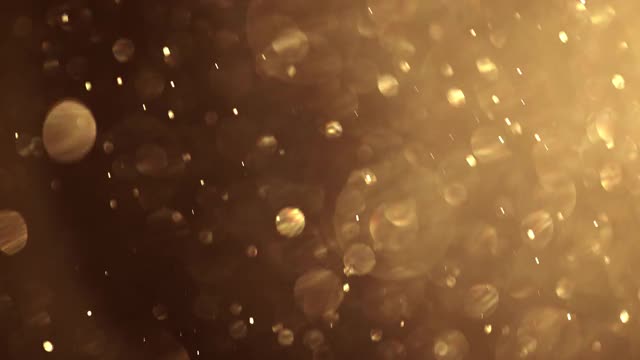 金粉颗粒在空气中飞扬。闪闪发光的黄金散景背景。视频素材