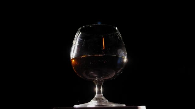 将白兰地从瓶中倒入玻璃杯中，以木色为背景。视频下载