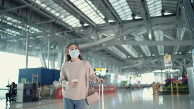 年轻的女旅行者戴着外科口罩，在电子时刻表上检查登机时间视频下载