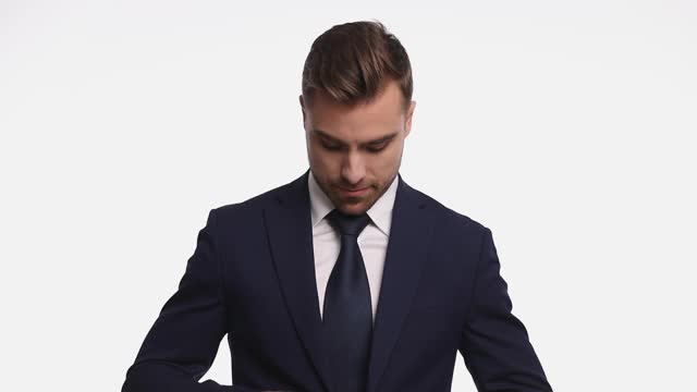 英俊的年轻人穿着深蓝色西装微笑着，手指交叉，交叉着手臂，扣着扣子，孤立地站在工作室的白色背景上视频下载