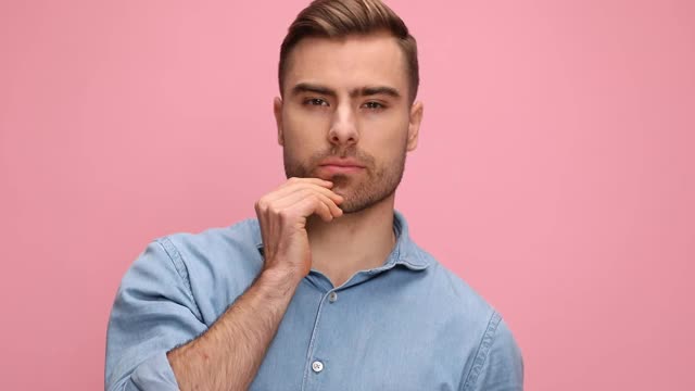 性感的年轻休闲男子在牛仔衬衫得到手指穿过头发，在一个诱惑的方式握着双手后脖子和在工作室的粉红色背景摆姿势视频素材