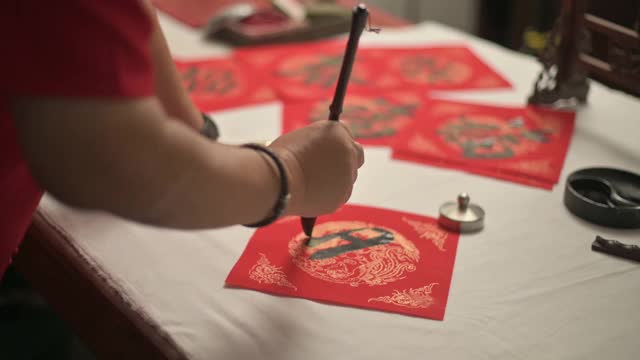 亚洲华人男性练习书法的手，为即将到来的中国新年庆祝家庭装饰目的繁荣和良好的措词写在一张红色的纸上视频素材