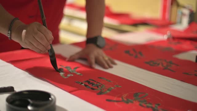 亚洲华人男性练习书法的手，为即将到来的中国新年庆祝家庭装饰目的繁荣和良好的措词写在一张红色的纸上视频下载