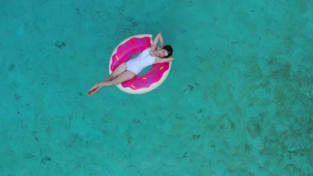 鸟瞰图一个迷人的女人浮动与游泳环在水晶清澈的大海视频下载