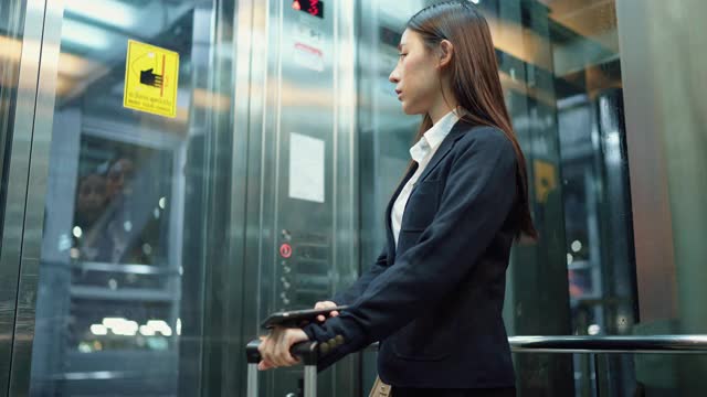 年轻的女秘书穿着正装在机场的电梯里使用智能手机视频下载