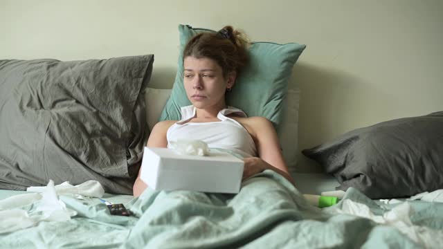 一位病人躺在床上，用电视遥控器切换频道视频素材
