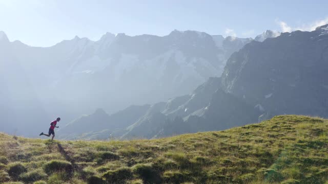 越野选手沿着长满草的山脊奔跑，后面是白雪覆盖的山峰。视频下载
