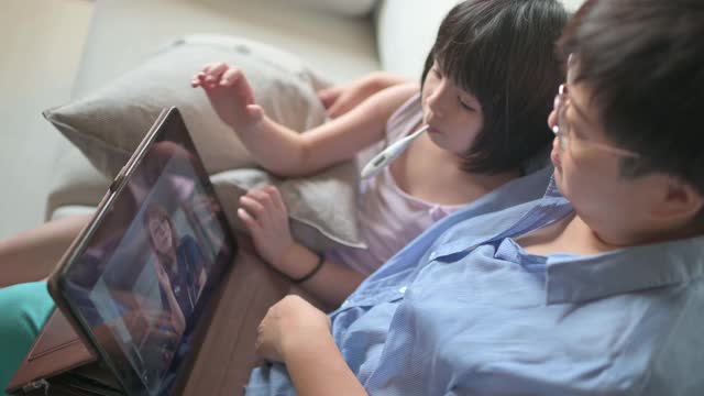 远程医疗亚洲华人母亲使用数字平板与医生儿科医生沟通她的女儿生病后，给她的女儿体温视频素材