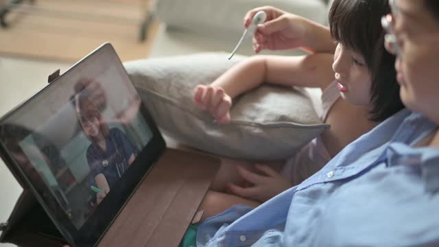 远程医疗亚洲华人母亲使用数字平板与医生儿科医生沟通她的女儿生病后，给她的女儿体温视频素材