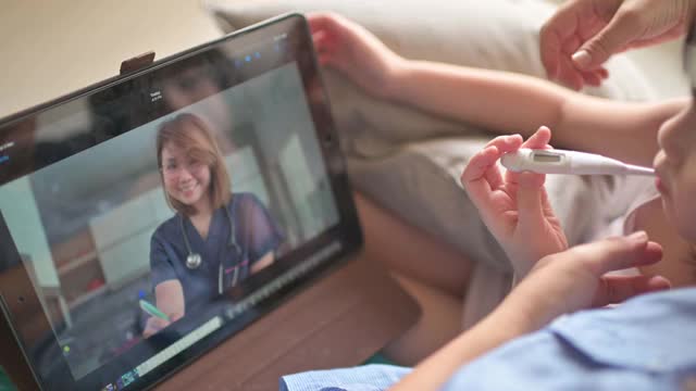 远程医疗亚洲华人母亲使用数字平板与医生儿科医生沟通她的女儿生病后，给她的女儿体温视频下载