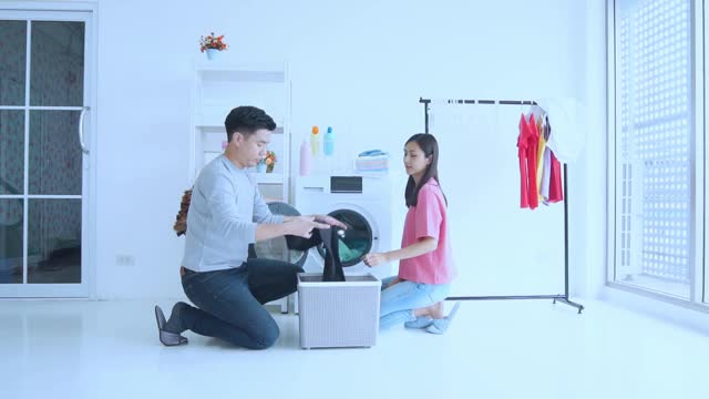 年轻夫妇在家里一起用自动洗衣机洗衣服和毛巾，他们一起打扫家里视频下载