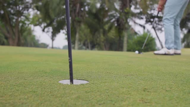 高尔夫球手在绿色的高尔夫球场上把球打到洞中，取出球并将球带回他的原点视频素材