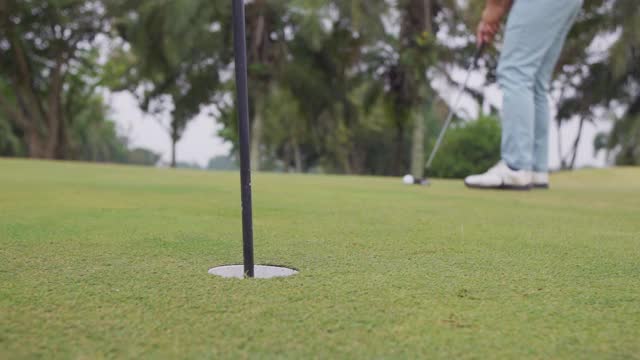 高尔夫球手在绿色的高尔夫球场上把高尔夫球打入洞中视频素材