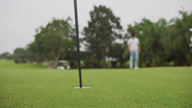 高尔夫球手在绿色的高尔夫球场上把高尔夫球打入洞中视频素材