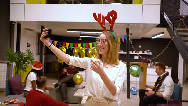 快乐的年轻现代女企业家在办公室派对上穿着驯鹿的鹿角自拍视频下载