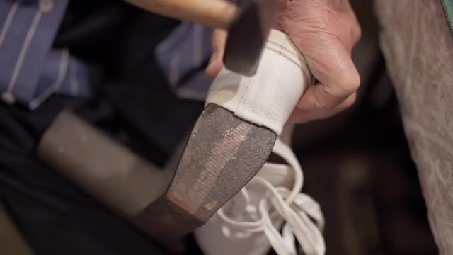 特写的旧鞋匠的手使用铁锤和修理白色运动鞋在车间。高级鞋匠使用金属工具软化运动鞋。工匠工匠的概念视频素材