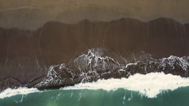 无人机拍摄的美丽的蓝绿色海浪在沙滩上破碎。航拍的金色海滩遇见深蓝色的海水和泡沫的波浪。高质量4k镜头视频素材
