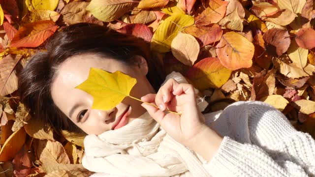 秋天的心情-年轻女子躺在公园里，拿着落叶享受秋天视频下载