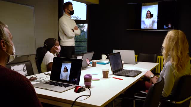 女性创意总监在董事会会议室的网络会议上向她的团队解释该项目，而团队中的所有人都戴着防护口罩以确保安全视频下载